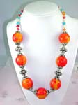 Wholesale fashion online jewelry importer supplying Large orange and red beaded necklace with silver plated chain connecting each bead and changing to small blue, orange, red, and whote beads around neck.